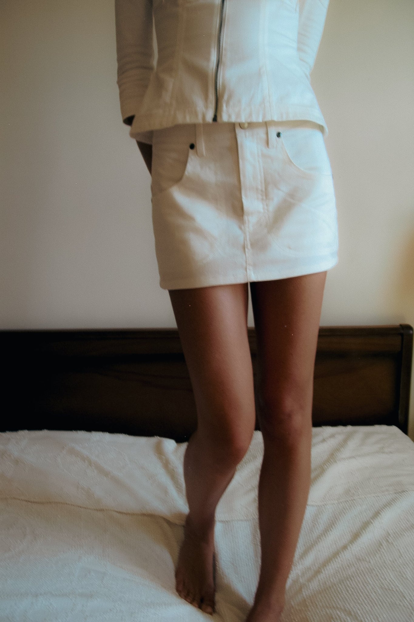 Person wearing a beige outfit standing on a bed with a neutral background
